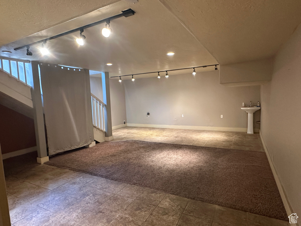 Below grade area with rail lighting, stairway, baseboards, and a textured ceiling