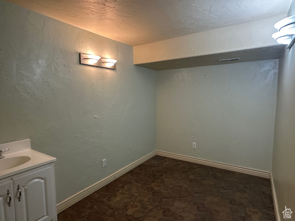 Finished basement featuring a sink, a textured wall, baseboards, and a textured ceiling