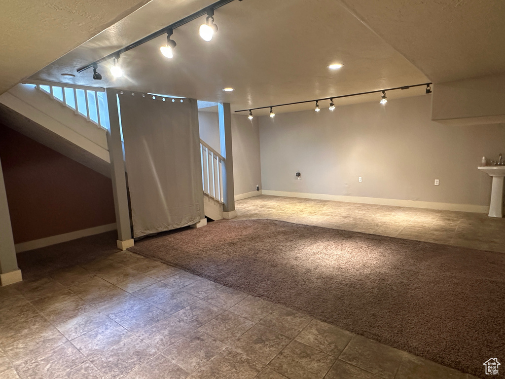 Below grade area featuring track lighting, stairs, and baseboards