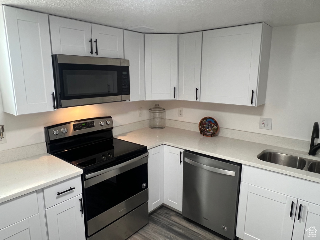 Kitchen featuring appliances with stainless steel finishes, a textured ceiling, dark wood-style floors, a sink, and light countertops