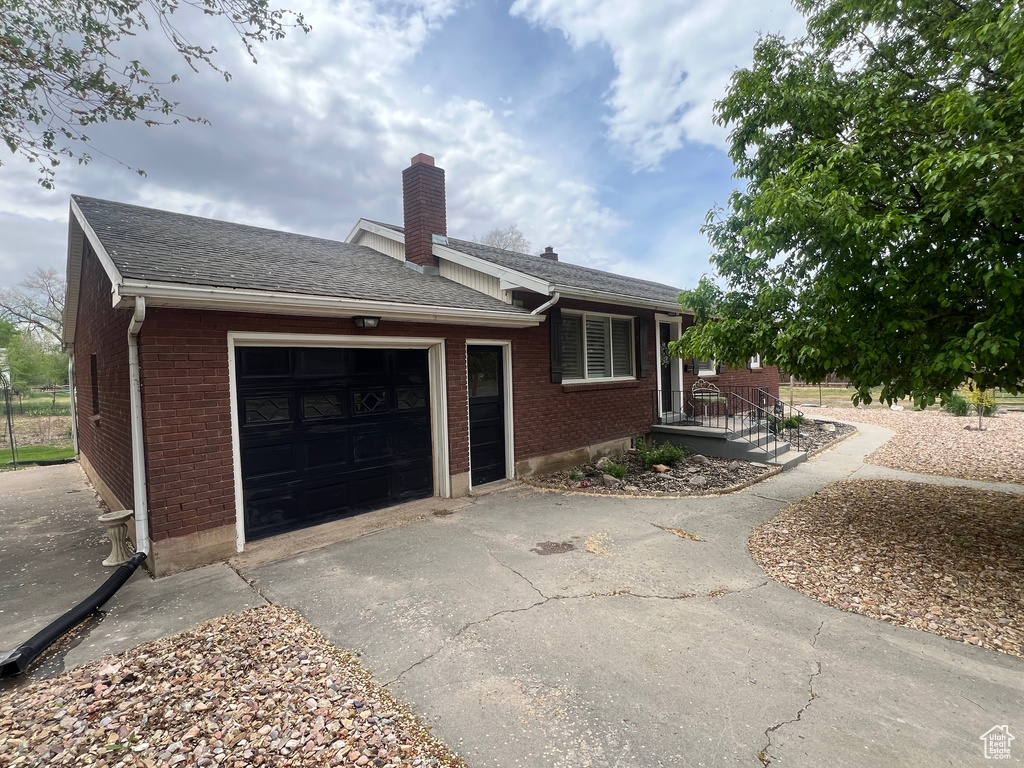 View of side of property featuring brick siding, an attached garage, a chimney, and driveway