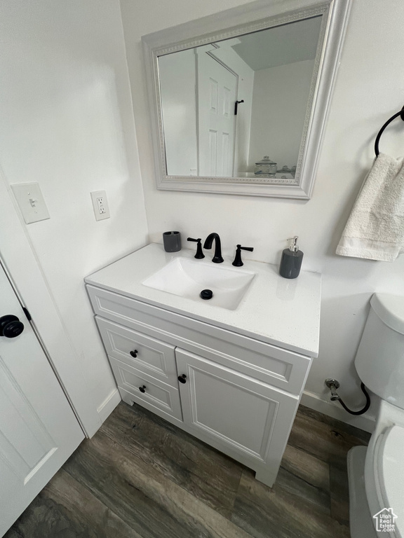 Half bathroom with toilet, wood finished floors, vanity, and baseboards