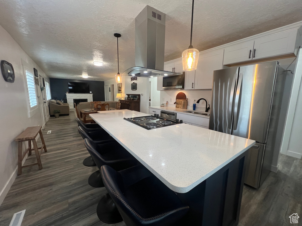 Kitchen featuring island range hood, appliances with stainless steel finishes, a textured ceiling, a sink, and dark wood-style flooring