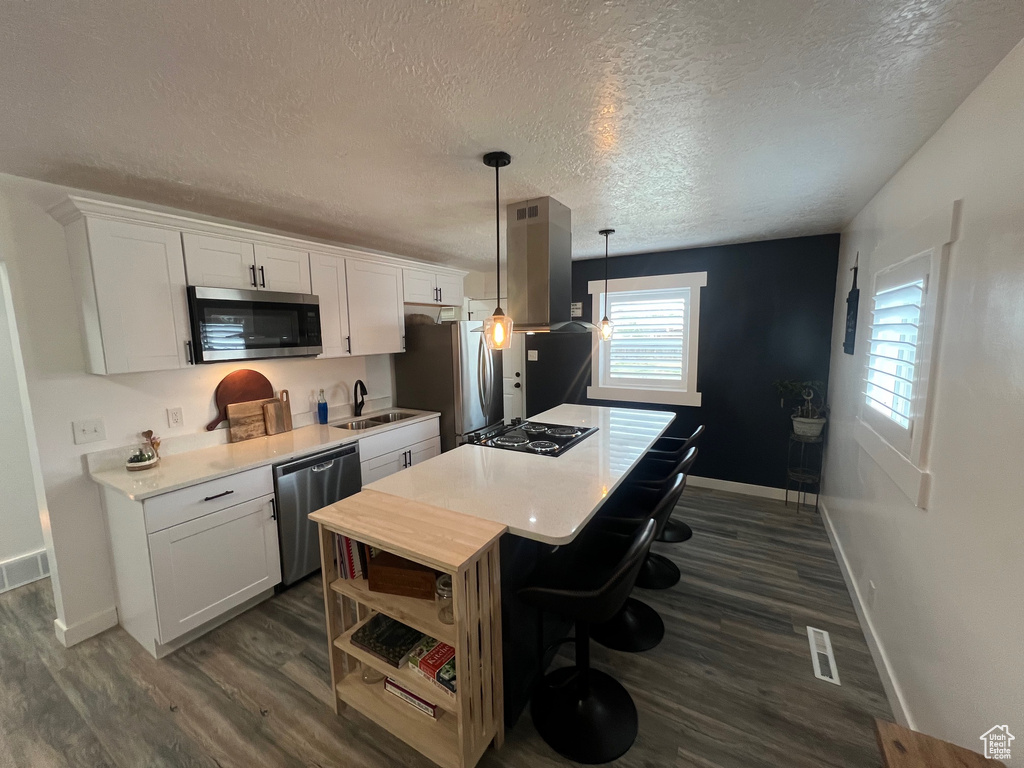 Kitchen featuring appliances with stainless steel finishes, baseboards, a center island, white cabinetry, and a textured ceiling