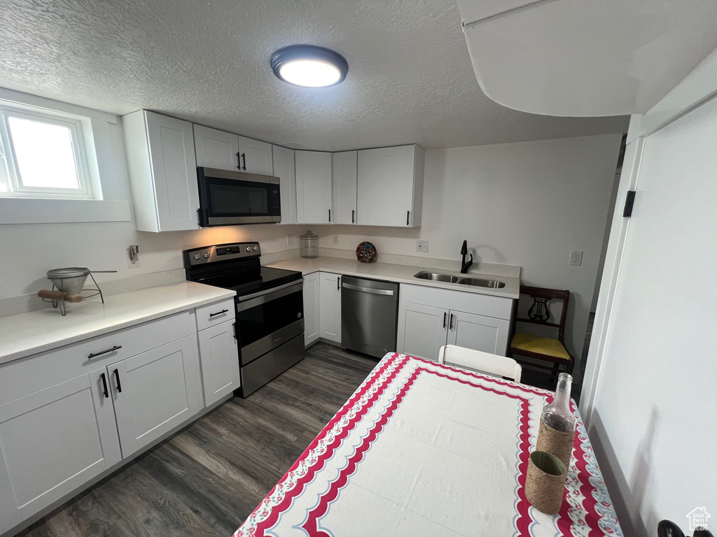 Kitchen featuring stainless steel appliances, a sink, dark wood finished floors, a textured ceiling, and light countertops