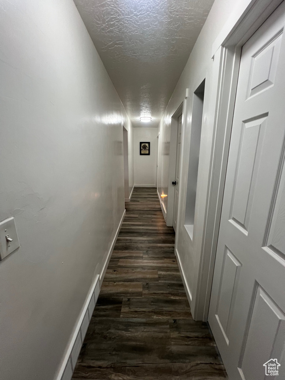 Hall with a textured ceiling, dark wood finished floors, and baseboards