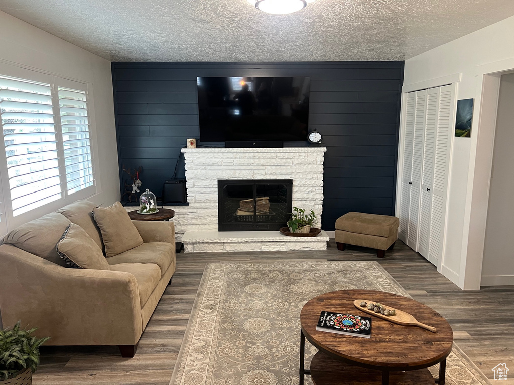 Living area featuring a textured ceiling, wood finished floors, a stone fireplace, and baseboards