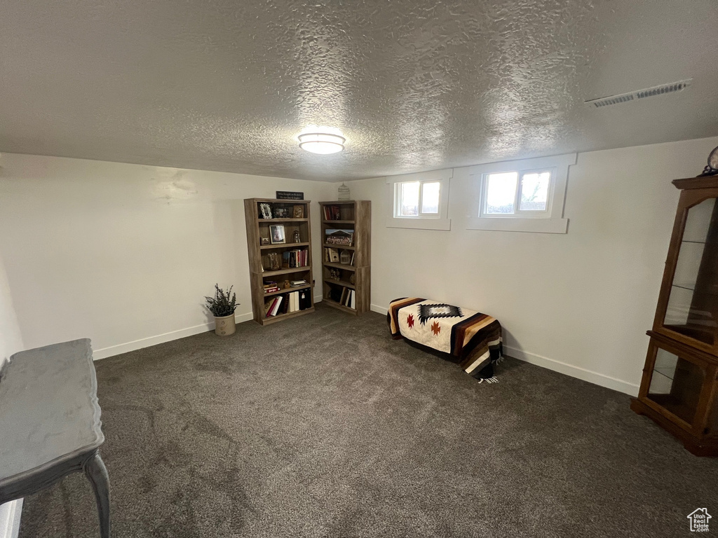 Basement with a textured ceiling, dark carpet, and baseboards