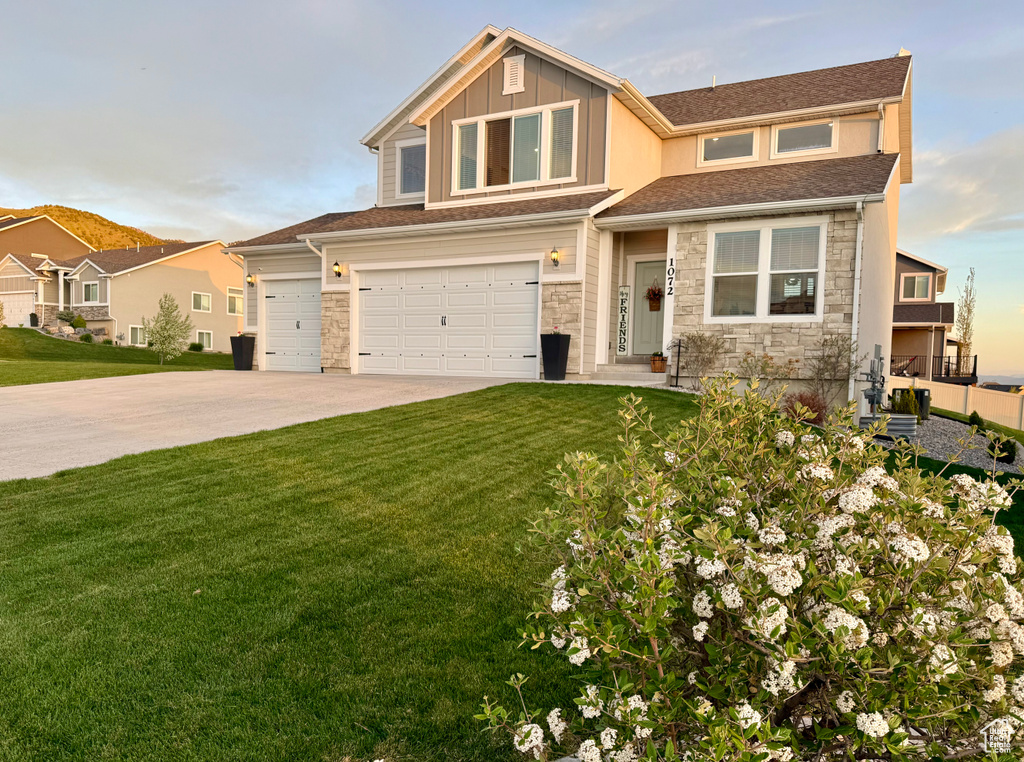View of front facade with stone siding, a front lawn, driveway, an attached garage, and board and batten siding