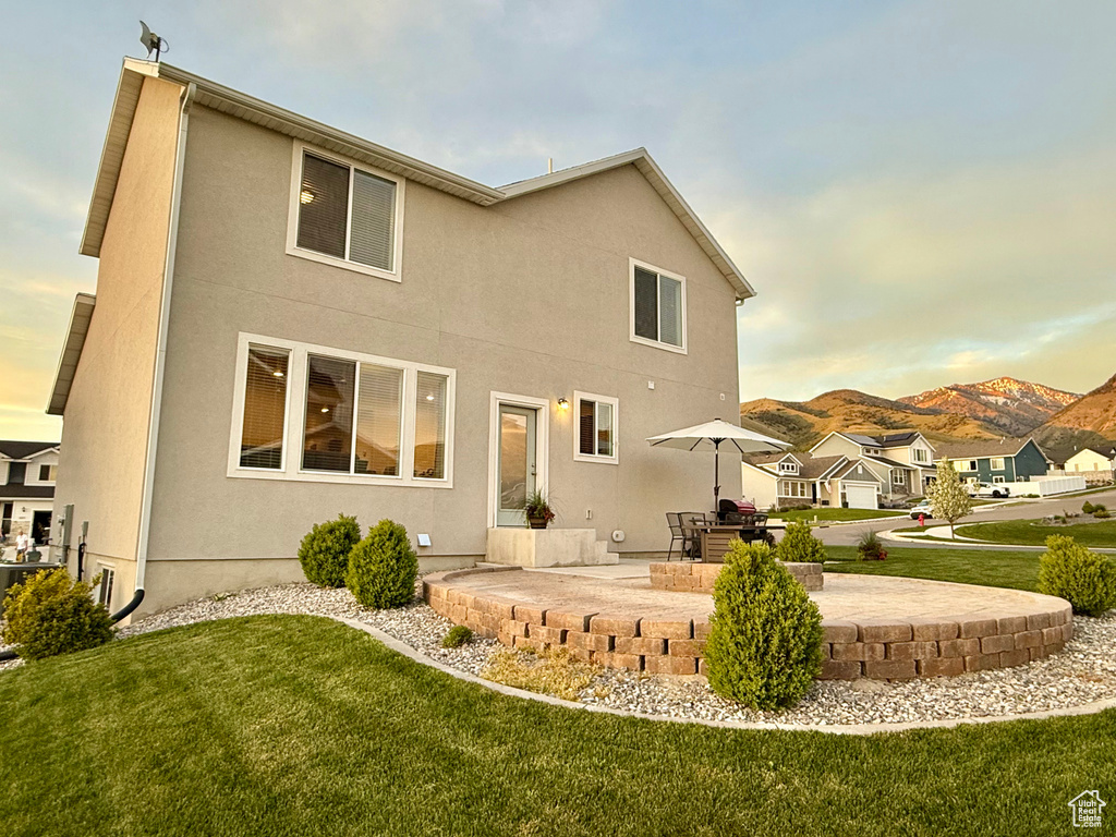 Back of property at dusk with a patio area, a lawn, stucco siding, and a mountain view