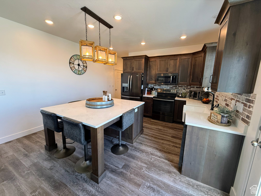 Kitchen featuring black fridge with ice dispenser, stainless steel microwave, range with electric cooktop, dark wood-style floors, and light countertops
