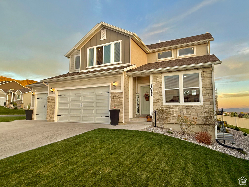 View of front facade with stone siding, a lawn, driveway, and a garage
