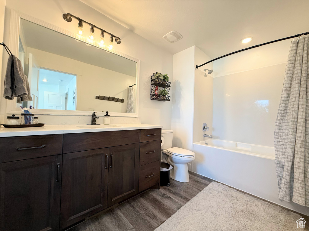Bathroom with wood finished floors, toilet, shower / bath combination with curtain, and vanity