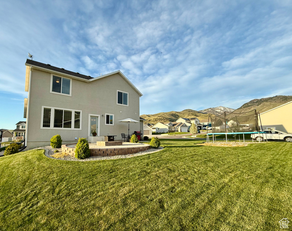 Rear view of house featuring a lawn, a patio area, a trampoline, and a mountain view