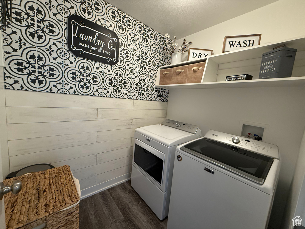 Clothes washing area featuring washing machine and clothes dryer, dark wood-type flooring, wooden walls, a textured ceiling, and baseboards