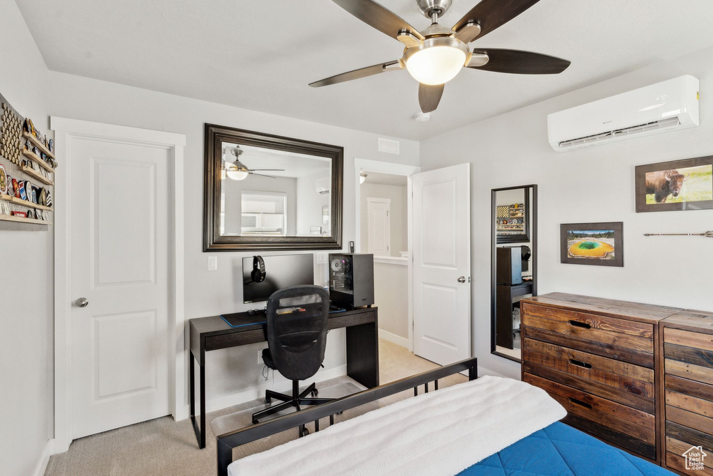 Bedroom with a wall unit AC, a desk, light colored carpet, baseboards, and a ceiling fan