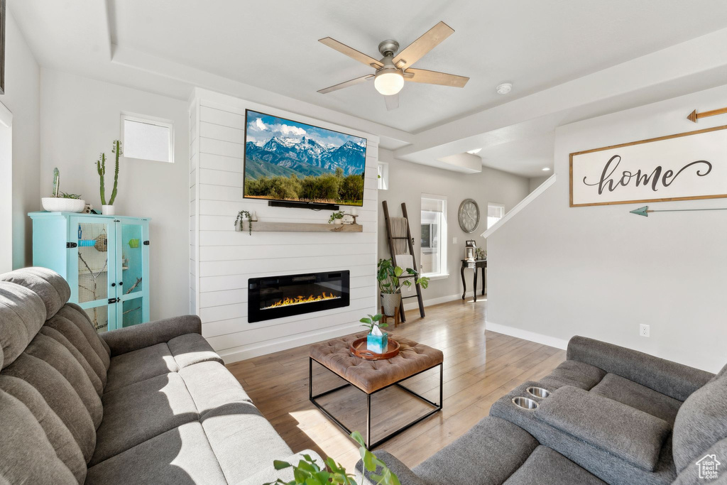 Living room with light wood finished floors, ceiling fan, healthy amount of natural light, and a fireplace
