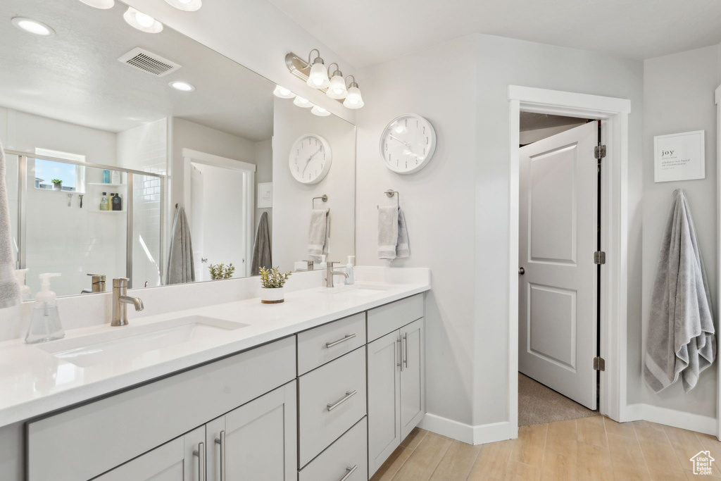 Full bathroom featuring wood finished floors, double vanity, a stall shower, recessed lighting, and baseboards