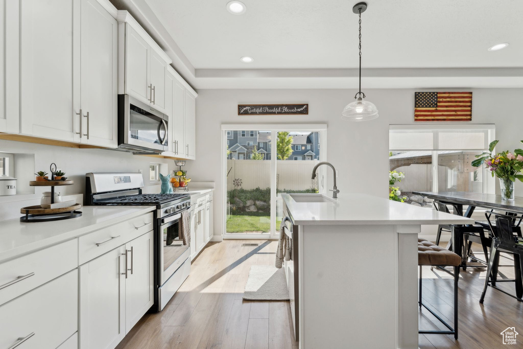 Kitchen with appliances with stainless steel finishes, a sink, light wood-type flooring, a breakfast bar, and recessed lighting