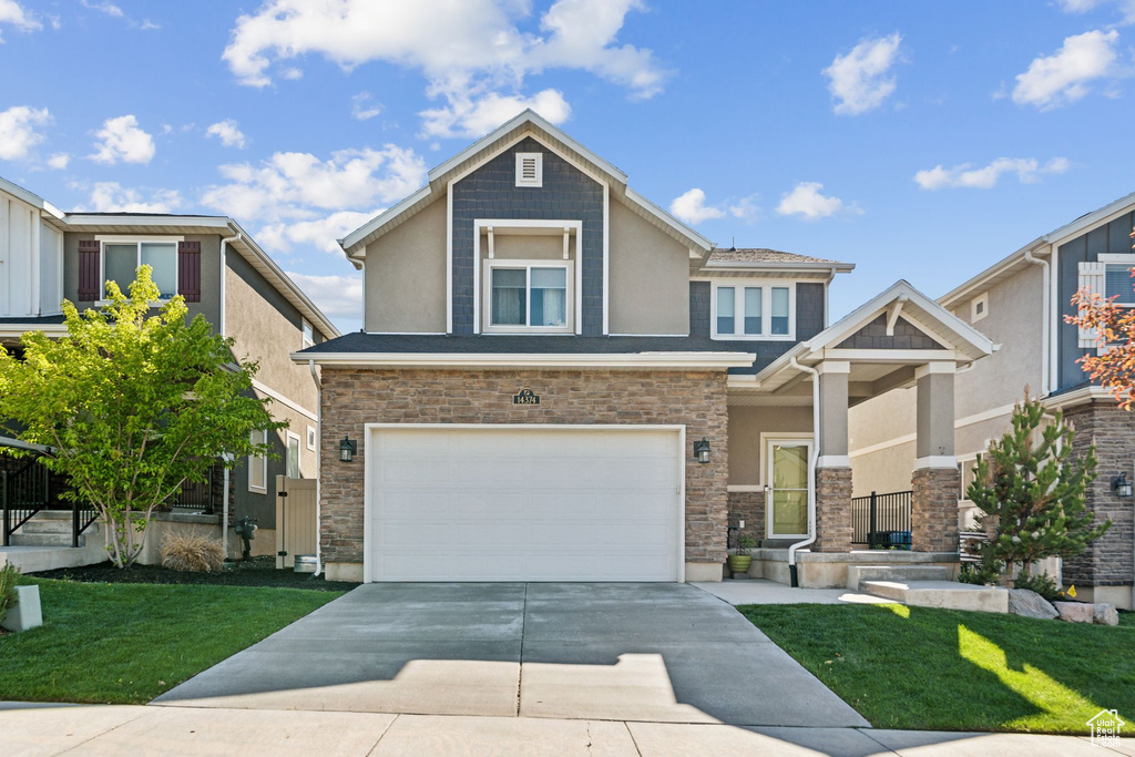 View of front of property with concrete driveway, stucco siding, an attached garage, a front yard, and stone siding