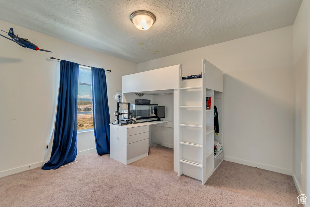 Unfurnished bedroom featuring light colored carpet, a textured ceiling, and baseboards