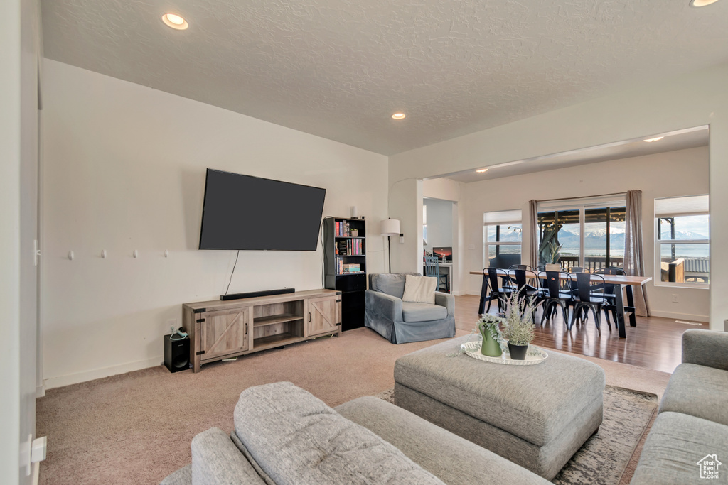 Living room with recessed lighting, a textured ceiling, baseboards, and light carpet