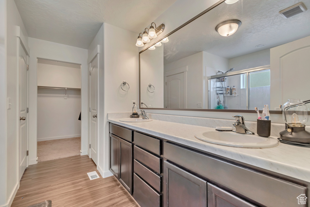 Full bath with a shower stall, double vanity, wood finished floors, and baseboards