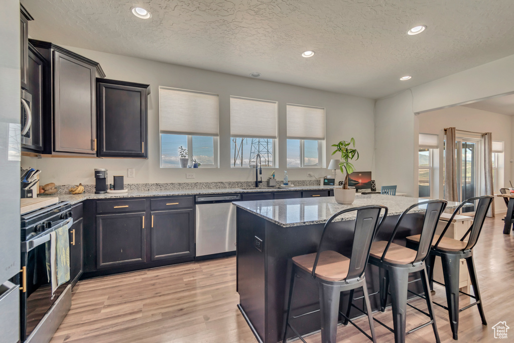 Kitchen featuring stainless steel appliances, a sink, a textured ceiling, light stone countertops, and a kitchen bar
