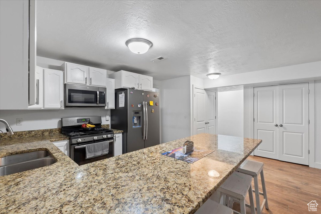Kitchen with appliances with stainless steel finishes, a sink, light stone counters, a breakfast bar, and white cabinets