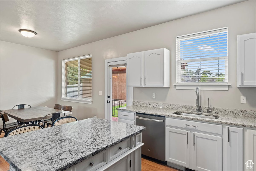 Kitchen featuring dishwasher, a sink, light wood finished floors, a kitchen island, and light stone countertops