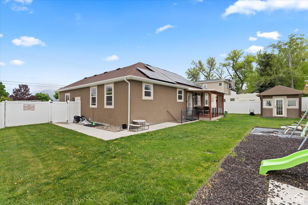 Rear view of property featuring solar panels, stucco siding, a patio, and an outdoor structure