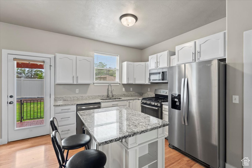 Kitchen with stainless steel appliances, a sink, white cabinetry, a kitchen breakfast bar, and light stone counters