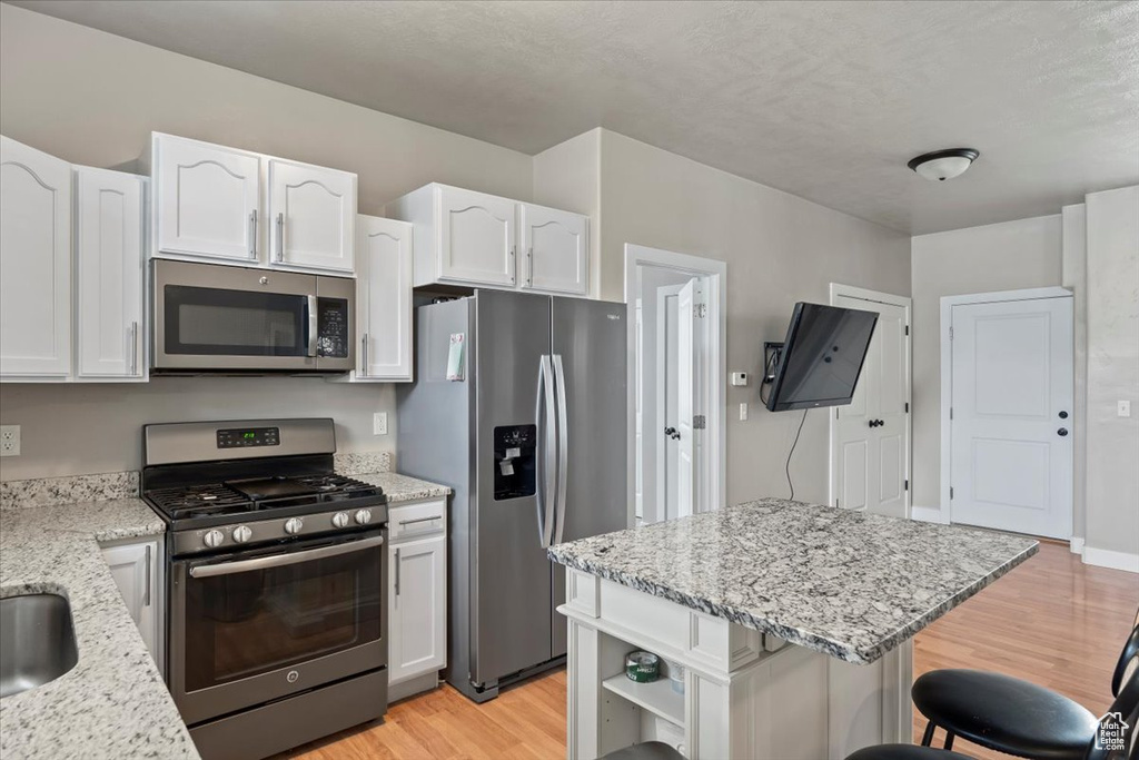 Kitchen with appliances with stainless steel finishes, light wood finished floors, white cabinetry, a kitchen breakfast bar, and light stone countertops