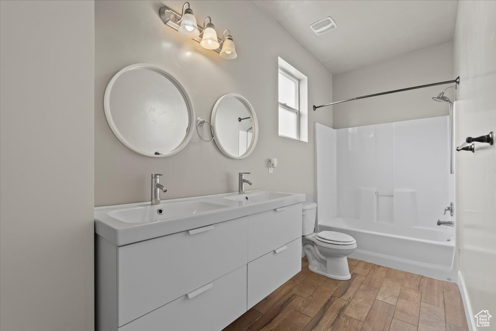 Full bathroom featuring wood finished floors, double vanity, toilet, and  shower combination