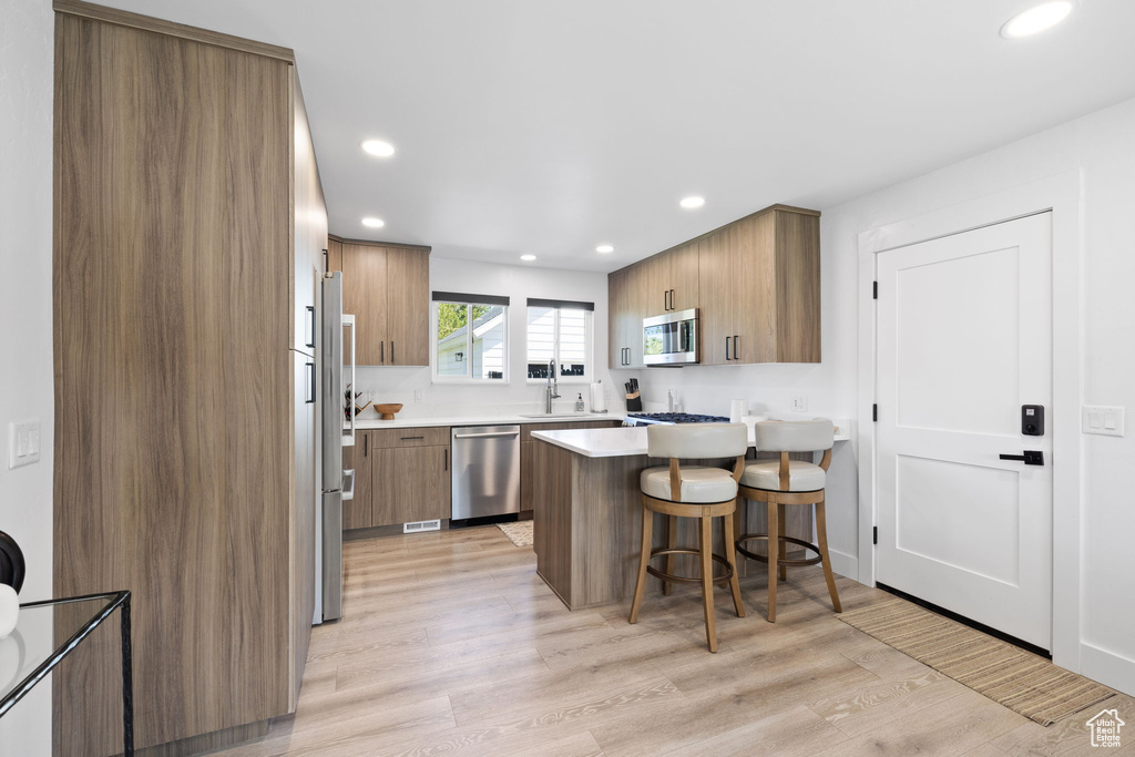 Kitchen with appliances with stainless steel finishes, a sink, a breakfast bar, a peninsula, and brown cabinetry