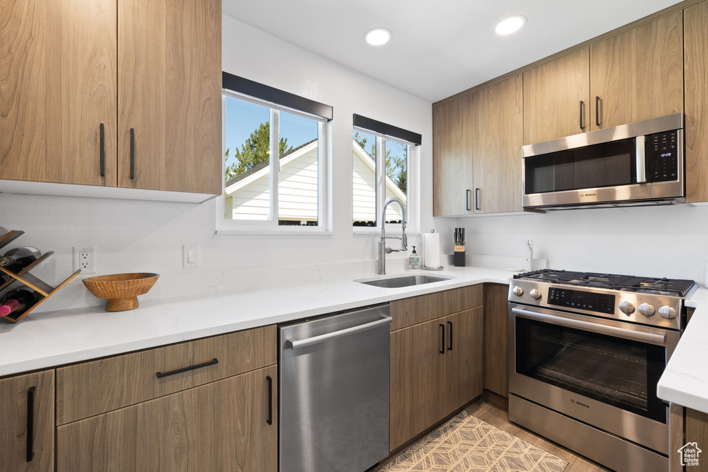Kitchen featuring stainless steel appliances, a sink, recessed lighting, light stone counters, and light wood-style flooring