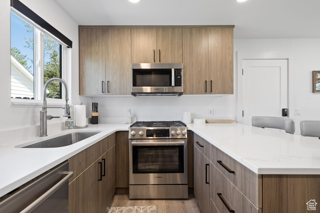 Kitchen with appliances with stainless steel finishes, a sink, a peninsula, light wood-style floors, and light stone counters