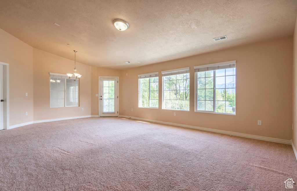 Carpeted empty room featuring a chandelier, baseboards, a textured ceiling, and lofted ceiling