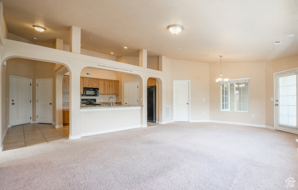 Unfurnished living room with light colored carpet, a chandelier, a sink, arched walkways, and baseboards