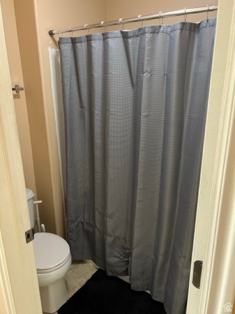 Bathroom with toilet, tile patterned floors, and curtained shower