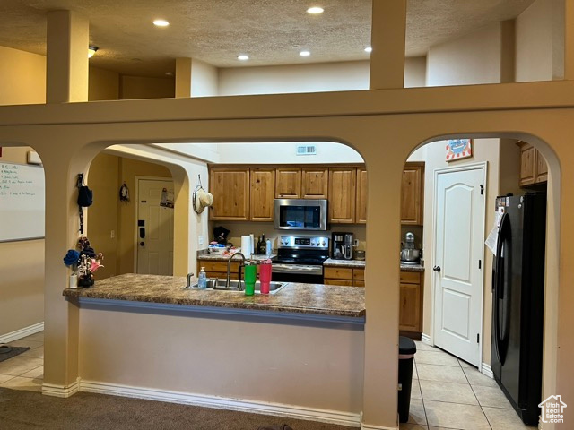 Kitchen featuring appliances with stainless steel finishes, brown cabinetry, light tile patterned flooring, arched walkways, and recessed lighting