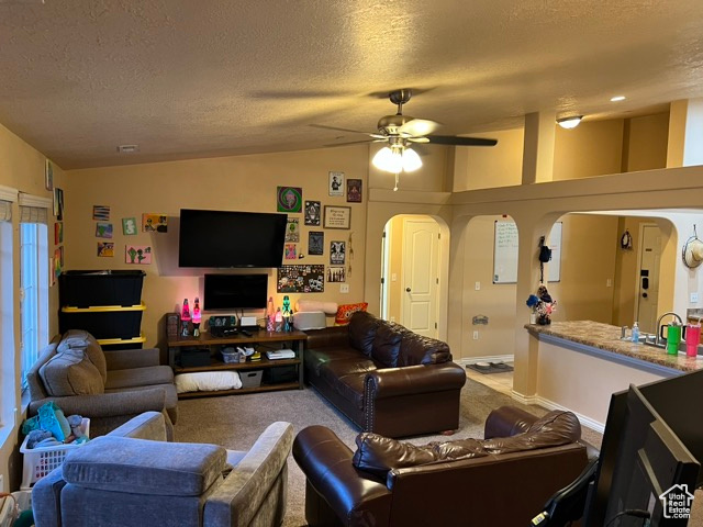 Carpeted living area with arched walkways, lofted ceiling, a textured ceiling, and ceiling fan