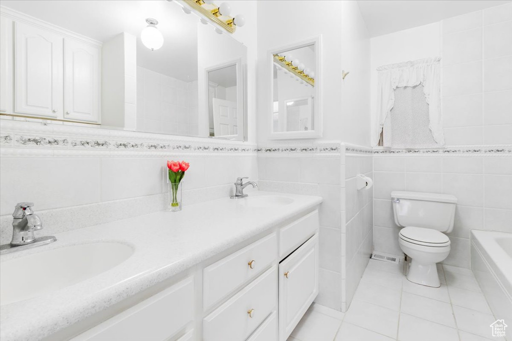 Bathroom featuring tile walls, tile patterned floors, toilet, double vanity, and a bathtub
