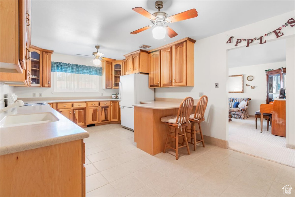 Kitchen featuring freestanding refrigerator, ceiling fan, a breakfast bar, and glass insert cabinets