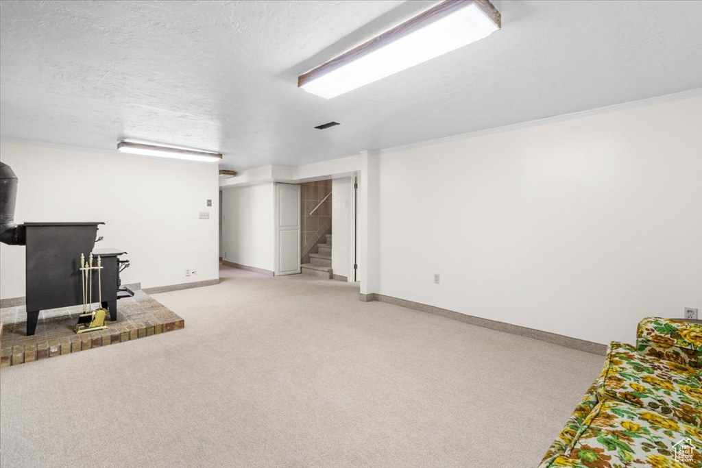 Finished basement featuring a wood stove, stairway, baseboards, light colored carpet, and a textured ceiling