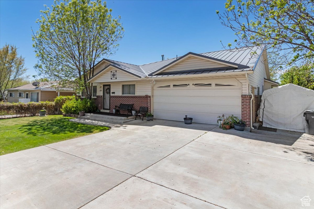 Ranch-style home featuring brick siding, an attached garage, driveway, a standing seam roof, and a front lawn