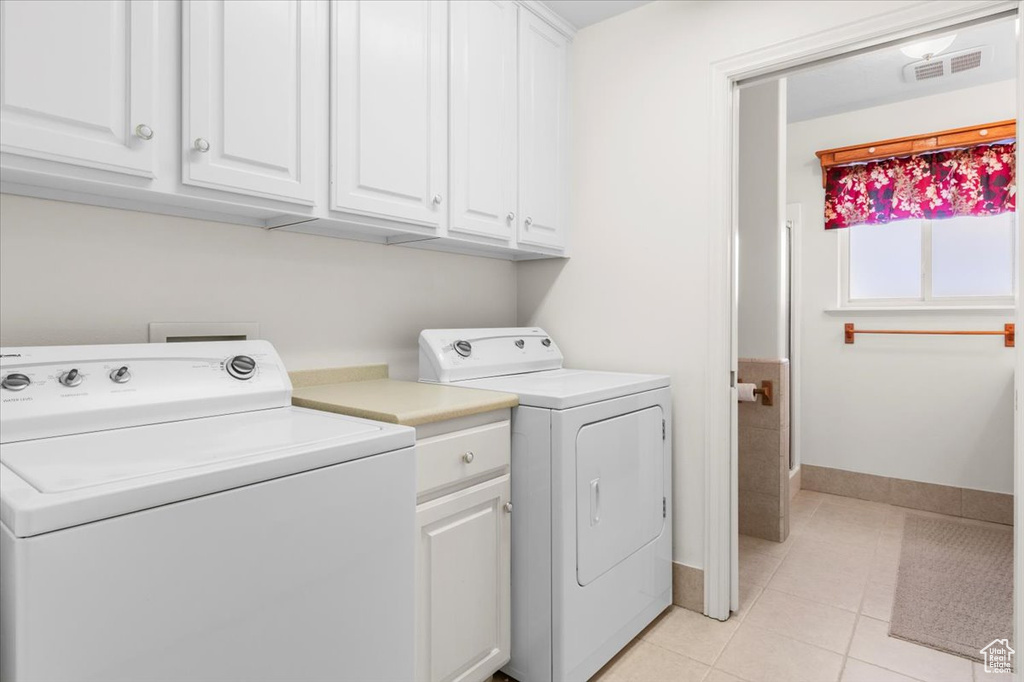 Clothes washing area with washer and clothes dryer, cabinet space, light tile patterned floors, and baseboards