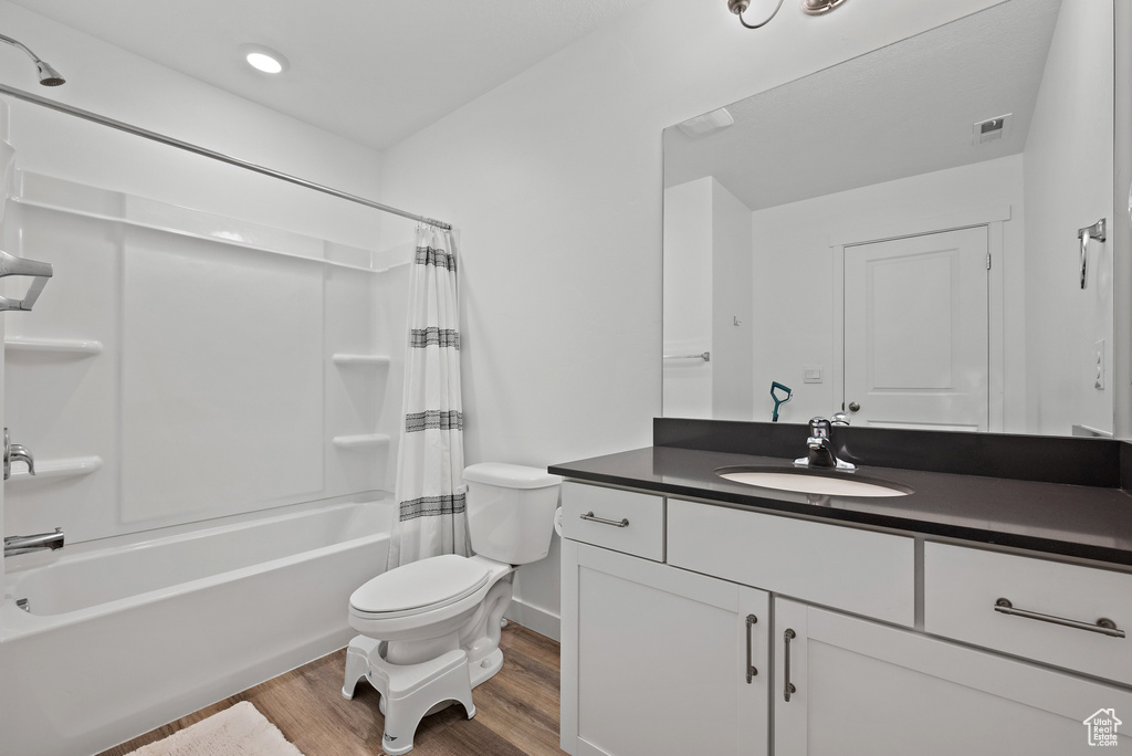 Bathroom with wood finished floors, toilet, vanity, shower / bathtub combination with curtain, and baseboards