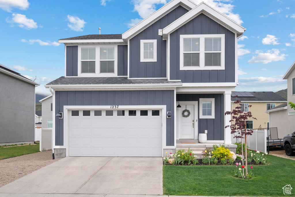 View of front facade featuring board and batten siding, driveway, a front yard, and a garage