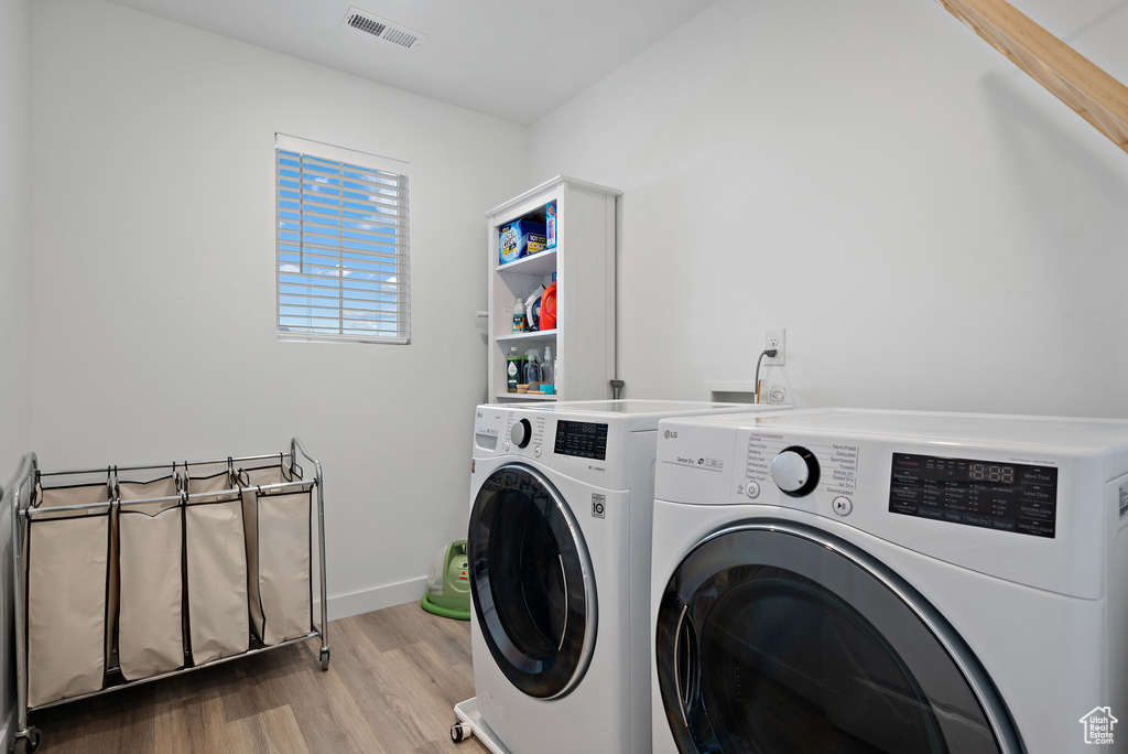Clothes washing area with independent washer and dryer and wood finished floors